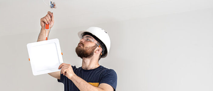 Electrician builder worker in a white helmet, installation of lamps at height copy space.