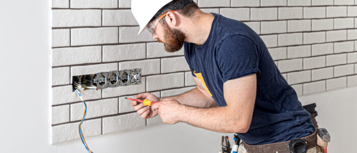 Electrician builder in a white helmet at work, installation of sockets, and switches.